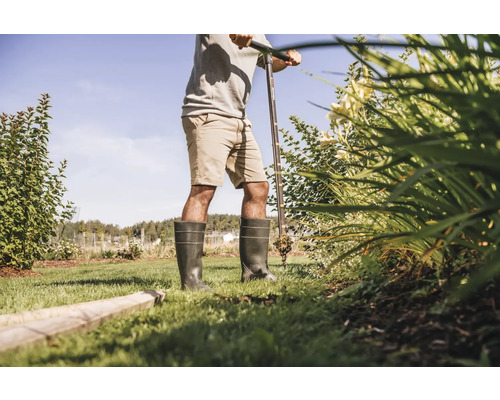 Une personne travaille dans le jardin avec une tarière et porte des bottes en caoutchouc.