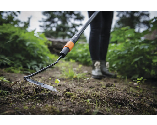 Personne utilisant une houe oscillante dans le jardin pour le désherbage.