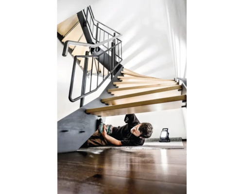 Un homme monte un escalier en colimaçon avec une perceuse sans fil et une lampe de travail