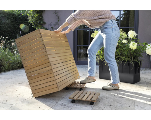 Une personne déplace un bac à plantes en bois sur une planche à roulettes dans le jardin.