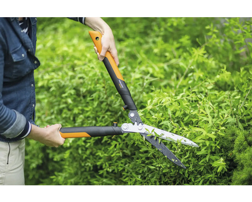 Person schneidet Hecke mit einer Heckenschere von Fiskars