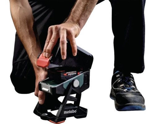 Une personne ouvre un projecteur de chantier à batterie Metabo pour remplacer la batterie.