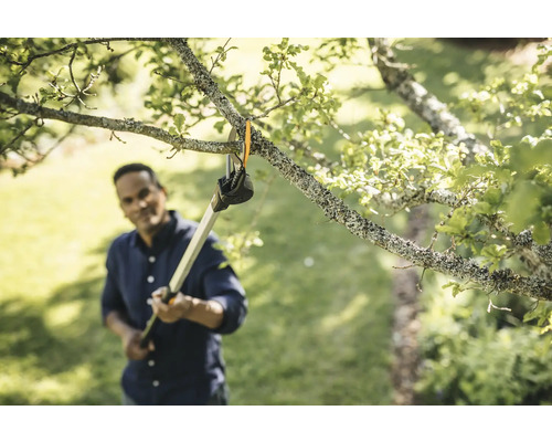 Un homme coupe des branches avec un ébrancheur dans le jardin.