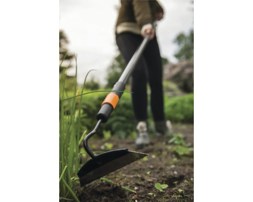Sarcloir de jardin avec manche télescopique utilisé dans le jardin.