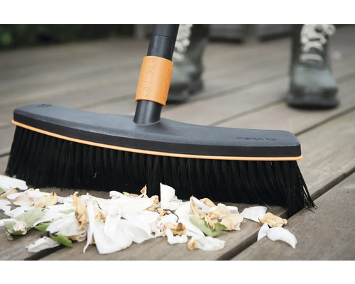 Balai pour nettoyer une terrasse en bois avec des restes de plantes.