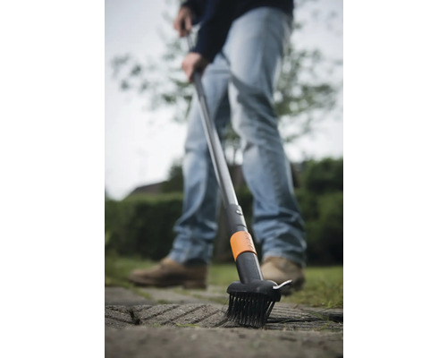 Un homme utilise une brosse à joints pour enlever les mauvaises herbes des pavés.