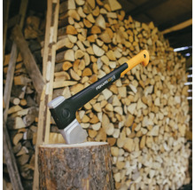 Hache de scission Fiskars sur un billot devant une pile de bois