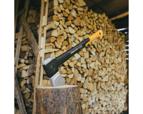 Hache de scission Fiskars sur un billot devant une pile de bois