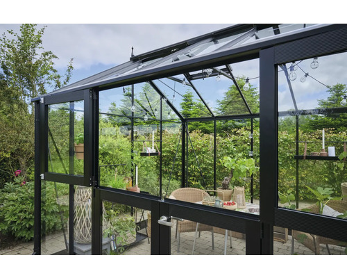 Serre avec parois en verre et cadre métallique, aménagée avec table et chaises.