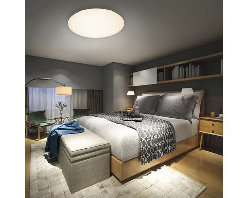 Schlafzimmer mit Bett, Nachttischen, Sitzbank, Teppich und Deckenleuchte