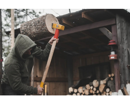 Person spaltet Holz mit einer Spaltaxt vor einem Holzschuppen.
