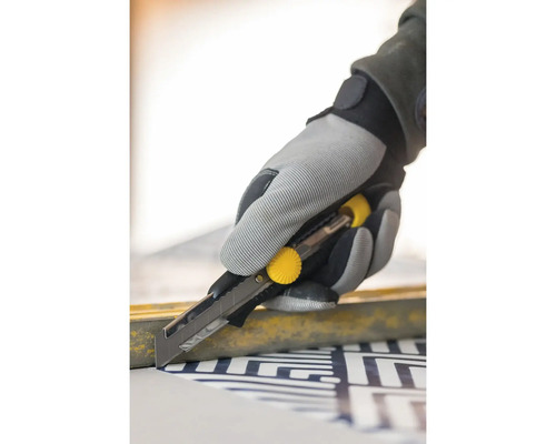 Eine Hand in einem Arbeitshandschuh verwendet ein Teppichmesser zum Schneiden von Material.
