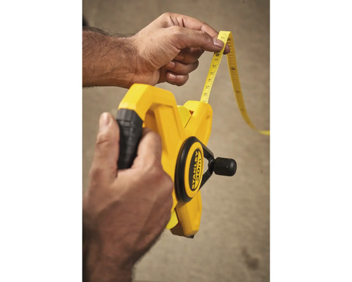 Une personne tient un mètre ruban jaune de 30 mètres de la marque Stanley.
