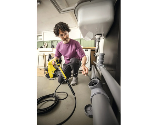 Un homme utilise un serpent de plomberie pour nettoyer un tuyau d''évacuation sous un lavabo.