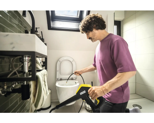 Un homme nettoie les toilettes avec un nettoyeur haute pression Kärcher dans la salle de bain.
