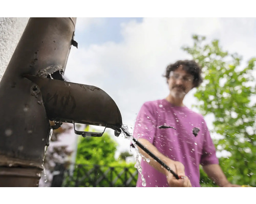 Un homme nettoie une gouttière bouchée avec un outil.