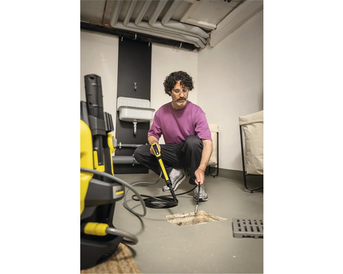 Un homme nettoie un drain avec un kit de nettoyage de canalisations et un nettoyeur haute pression dans une cave.