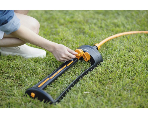 Person justiert einen Gartensprenger von Fiskars auf einer Rasenfläche.