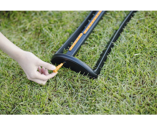 Ein Gartenregner wird mit einem Erdspieß im Gras befestigt.