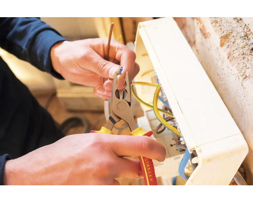 Ein Elektriker verwendet eine Zange, um ein Kabel in einem Verteilerkasten zu bearbeiten.