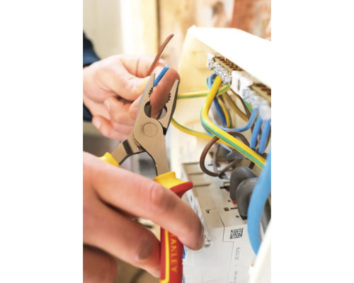 Elektriker bearbeitet Kabel mit einer Abisolierzange an einem Sicherungskasten