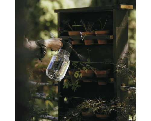 Eine Person giesst Pflanzen in einem Regal mit einer transparenten Sprühflasche.