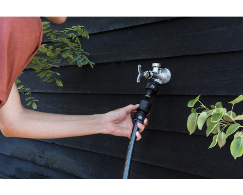 Une personne raccorde un tuyau d''arrosage à un robinet extérieur