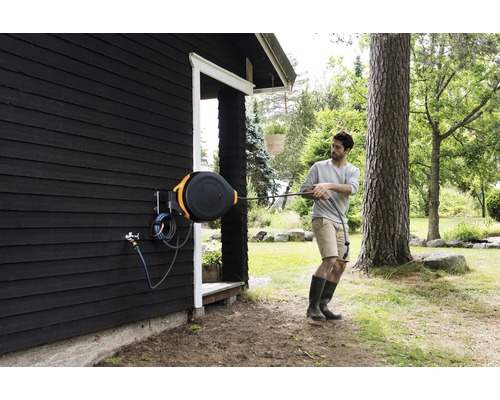 Person zieht einen Gartenschlauch von einer Schlauchbox an einer Hauswand