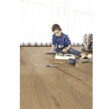 Kind malt auf einem Holzfußboden. Im Hintergrund befindet sich ein Plüschtier-Elefant.