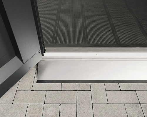 Bodenrampe Hörmann EcoStar Euroline 105,5 x 11 x 4 cm silber Detailansicht eines Schwellenprofils zwischen einer Tür und Pflastersteinen.