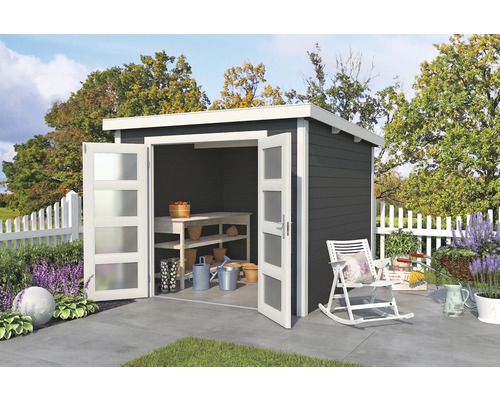 Abri de jardin avec double porte, établi et outils de jardin devant une clôture blanche