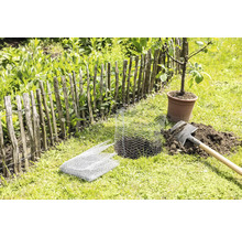 Scène de jardin avec clôture à lattes, bêche, grillage et arbre en pot