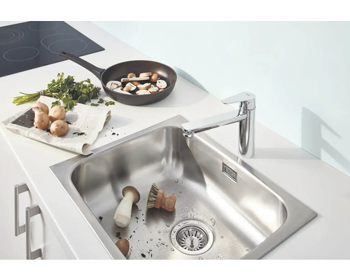 Évier en acier inoxydable avec robinet de cuisine, champignons, poêle à frire et herbes aromatiques sur un plan de travail