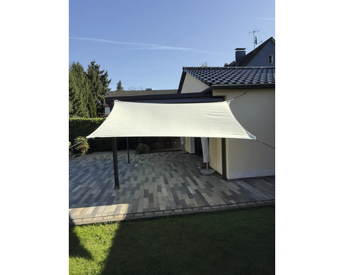 Voile d'ombrage rectangulaire au-dessus d'une terrasse avec des pavés et une pelouse.