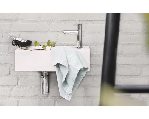 Waschbecken mit Armatur, Handtuch und Accessoires an einer Wand aus Ziegelsteinen