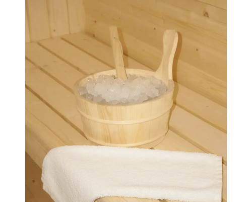Holzeimer mit Eis und Schöpfkelle in einer Sauna, neben einem Handtuch.