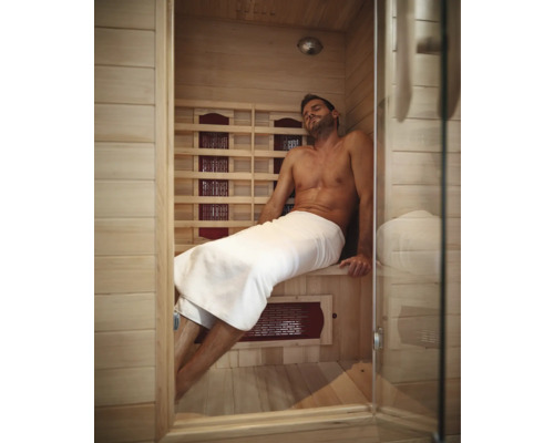 Mann entspannt in einer Infrarotsauna mit Holzwänden und Glastür