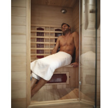 Mann entspannt in einer hellen Holz-Infrarotsauna mit Glastür