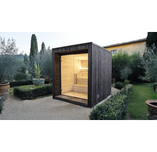 Moderne Außensauna aus dunklem Holz mit Glasfront und hellen Holzbänken in einer Gartenanlage.
