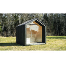 Modernes Gartensaunahaus mit dunkler Holzfassade, vollständiger Glasfront und Satteldach auf einer Wiese vor Bäumen.