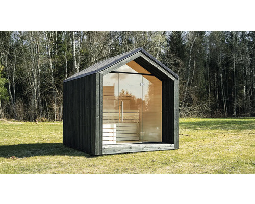 Modernes Gartensaunahaus mit dunkler Holzfassade, vollständiger Glasfront und Satteldach auf einer Wiese vor Bäumen.