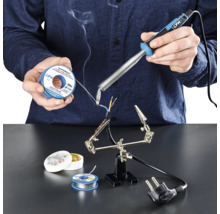 Person lötet mit Lötkolben, Lötzinn und Lötfett Kabel auf einer Arbeitsfläche.