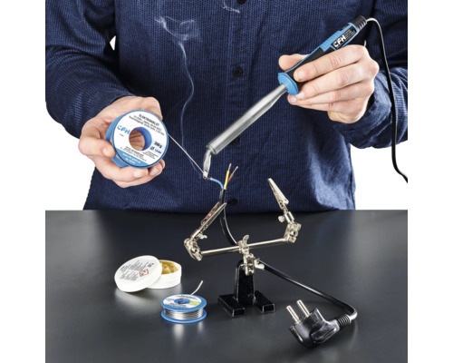 Person lötet mit Lötkolben, Lötzinn und Lötfett Kabel auf einer Arbeitsfläche.