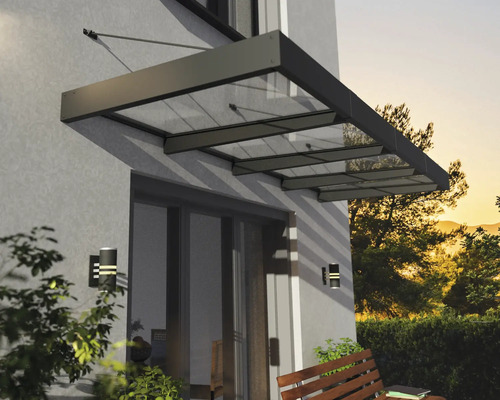Modernes Vordach aus Glas und Metall über einer Terrassentür an einer Hauswand mit Wandleuchten und einer Holzbank.