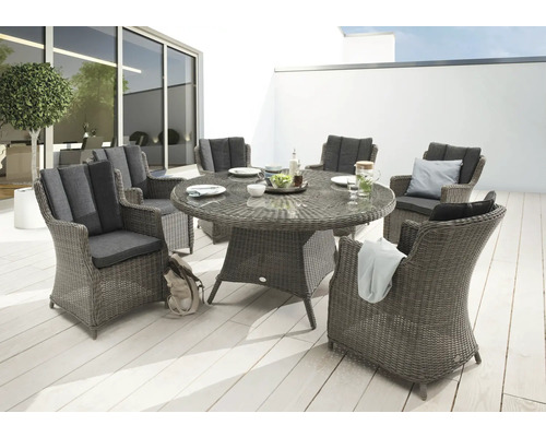 Gartenszene mit einem runden Esstisch aus Rattan und sechs passenden Sesseln mit Polsterauflagen auf einer Terrasse.