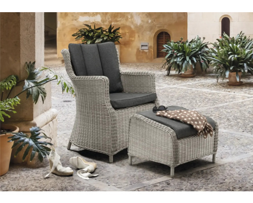 Geflochtener Sessel mit Fusshocker und grauen Polstern auf einer gepflasterten Terrasse.