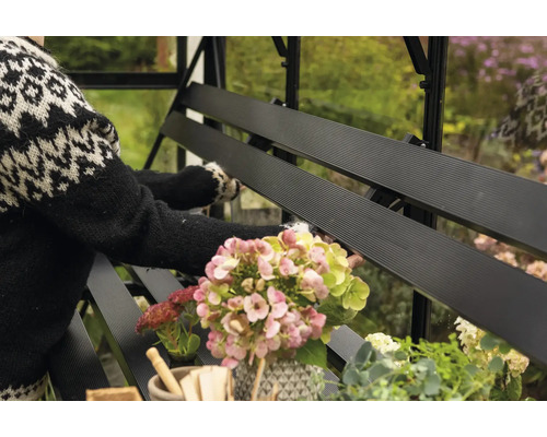Vue détaillée d'un banc de serre noir avec des fleurs et une personne en arrière-plan