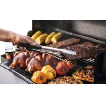 Scène de barbecue avec du poulet, des épis de maïs, des côtes levées, des poivrons et des pizzas retournés avec une pince à barbecue