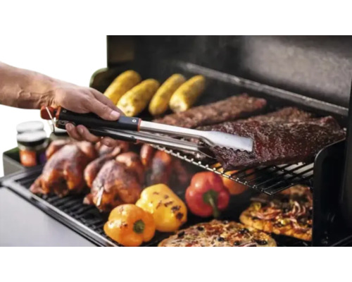 Scène de barbecue avec du poulet, des épis de maïs, des côtes levées, des poivrons et des pizzas retournés avec une pince à barbecue