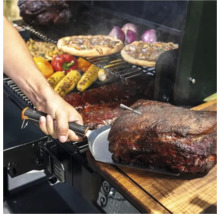 Scène de barbecue avec de la viande, des pizzas, des épis de maïs et des légumes préparés sur un gril. Une personne tient une spatule.